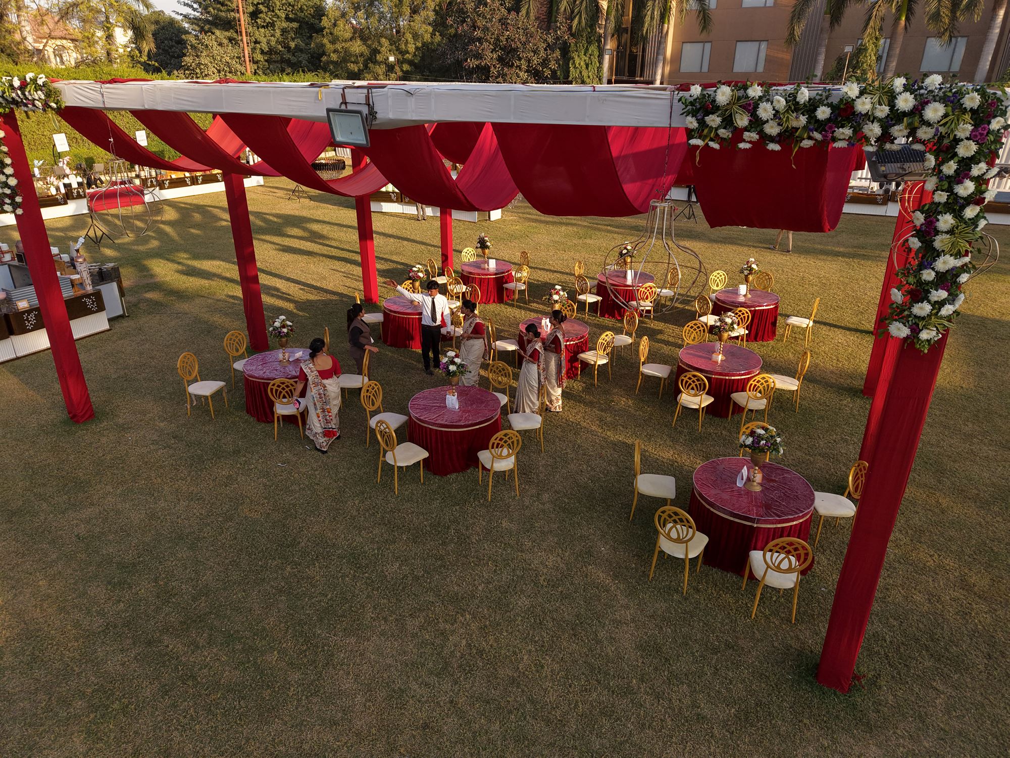 Red draped canopy over round dinner tables at golden hour with floral chandeliers