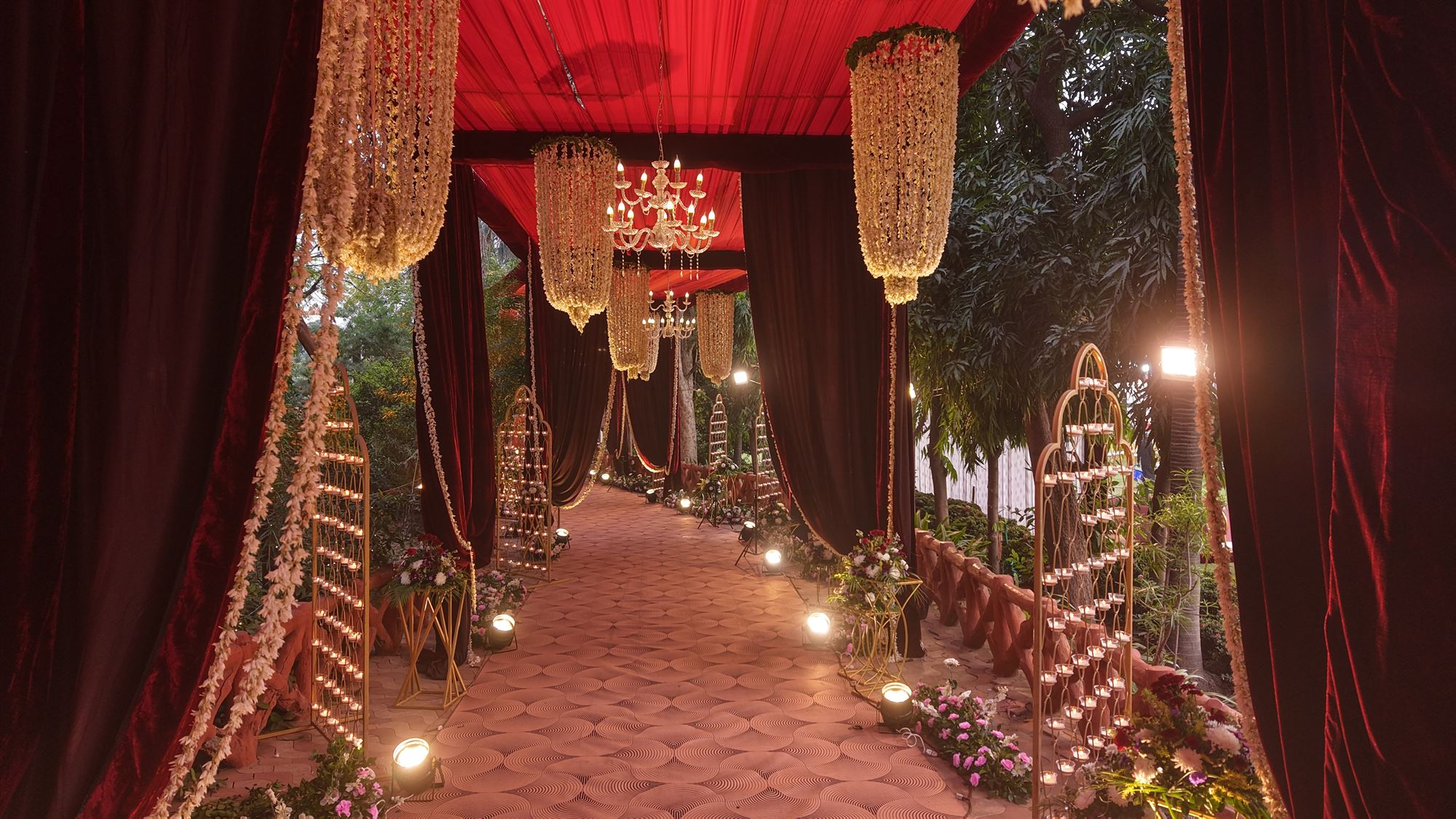 Crimson velvet walkway with jasmine garland chandeliers and candle lattice screens
