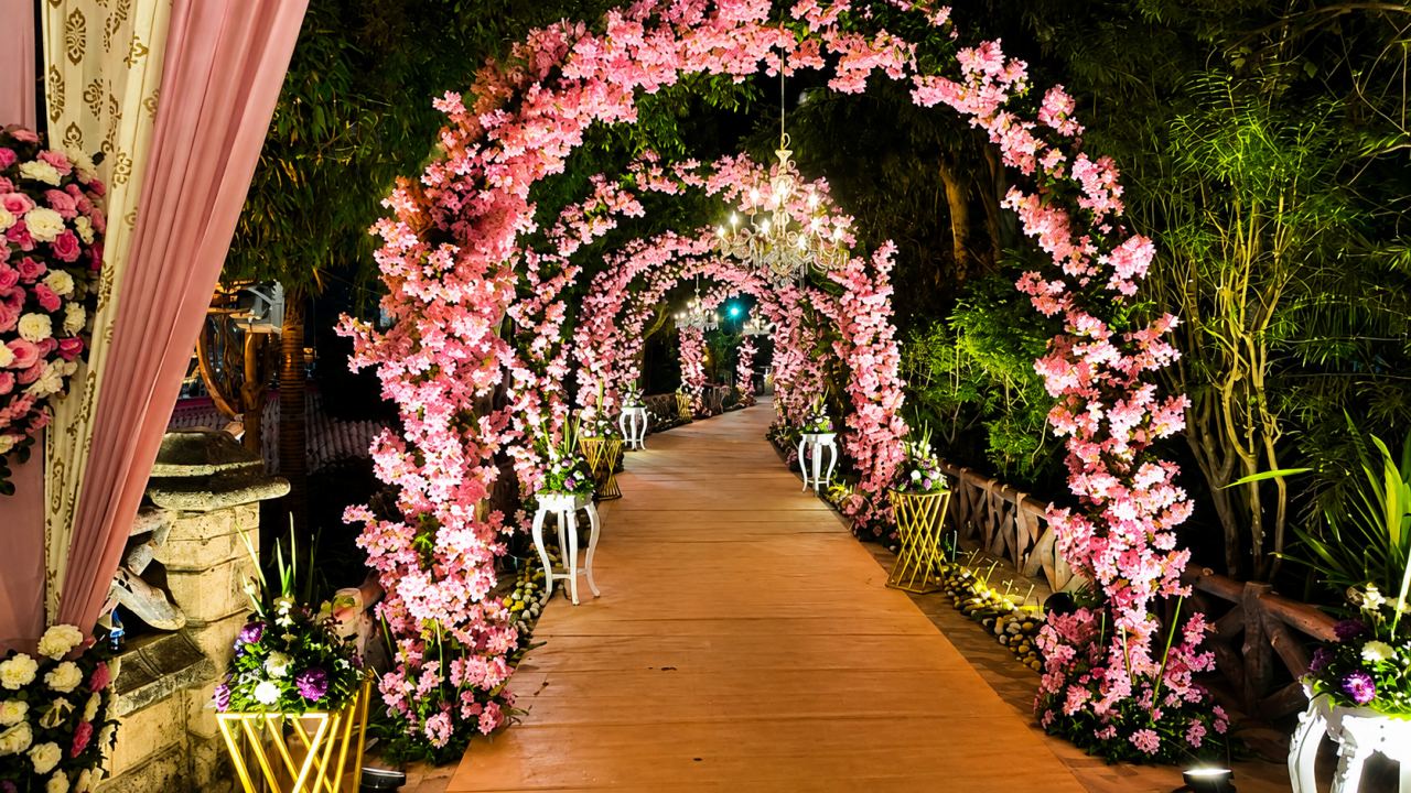 Wedding entrance pathway with fairy-light curtains, pampas grass and maroon pillars