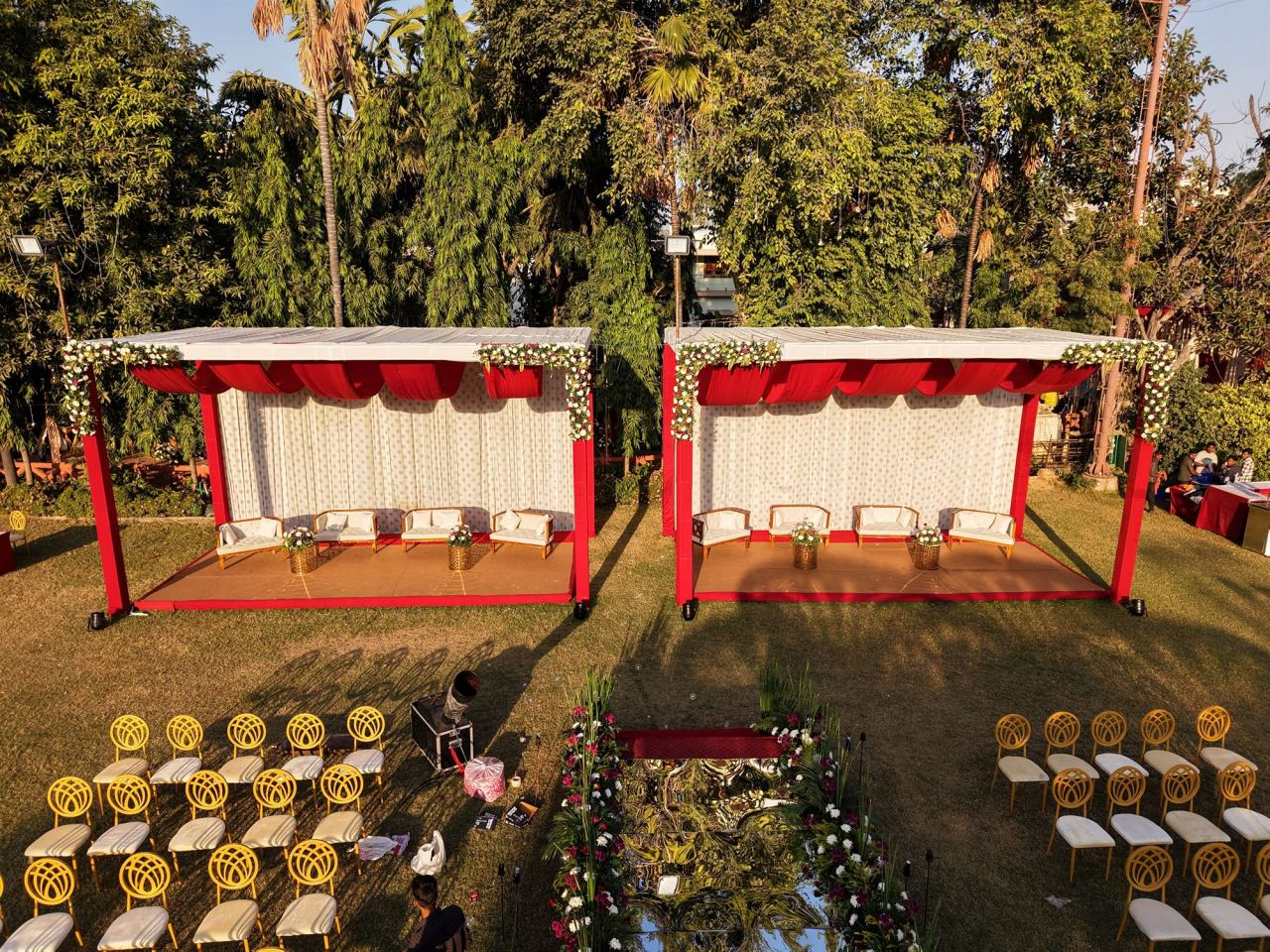 Twin red-canopy family pavilions with white lounge seating on a wedding lawn